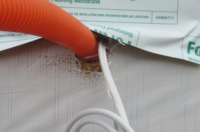 Close-up of an exterior wall penetration with incomplete house wrap around conduit during a pre-sheetrock home inspection in Manvel, Texas